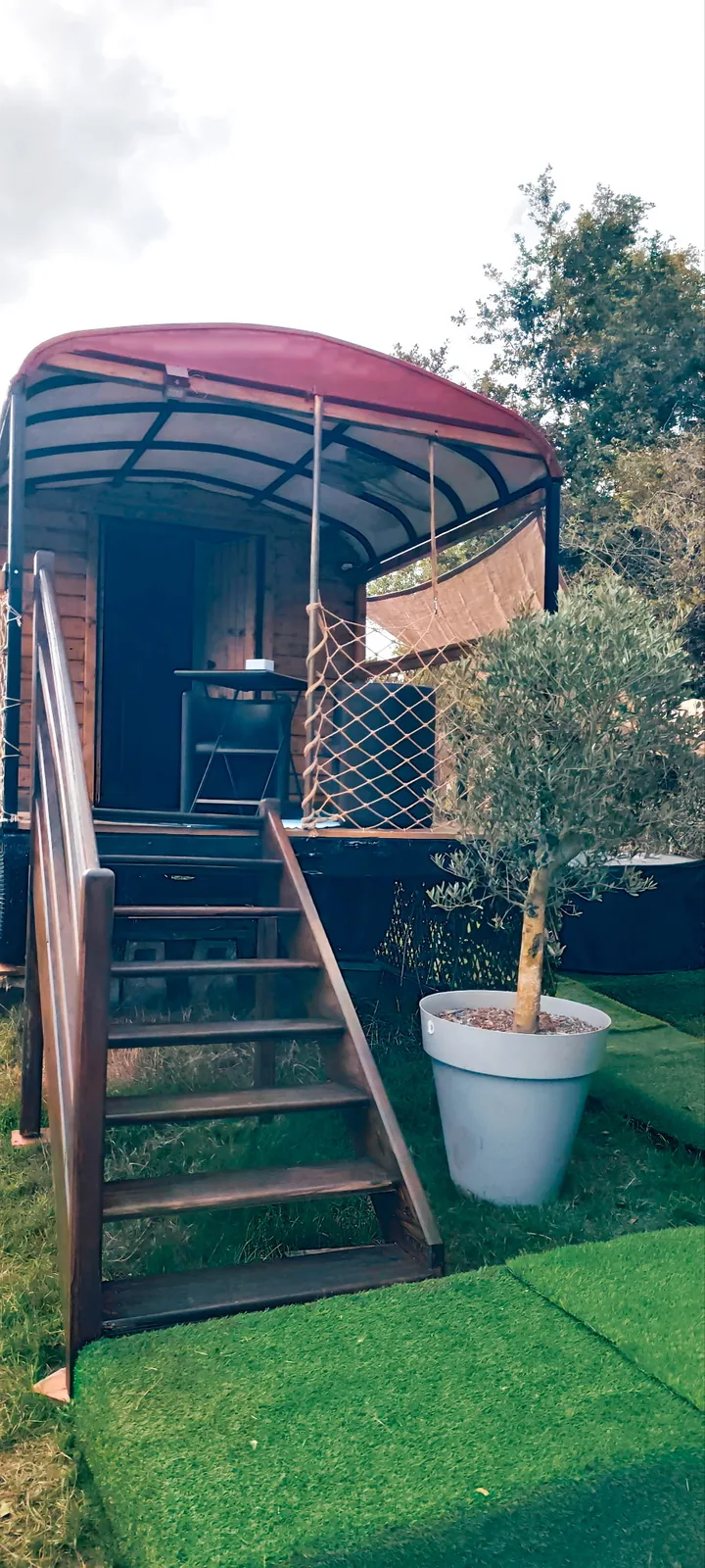 Le Luxury Circus — La roulotte vue du jardin, son toit rouge et son escalier de bois